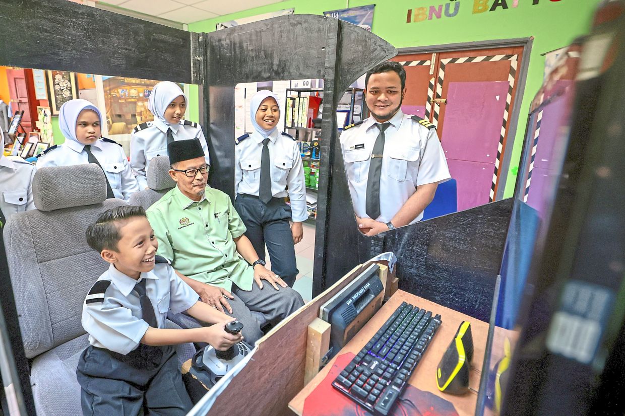 Azlan (seated) and Aeronautics Club coordinating teacher Tengku Ahmad Fareez watching a pupil do flight simulation exercises.