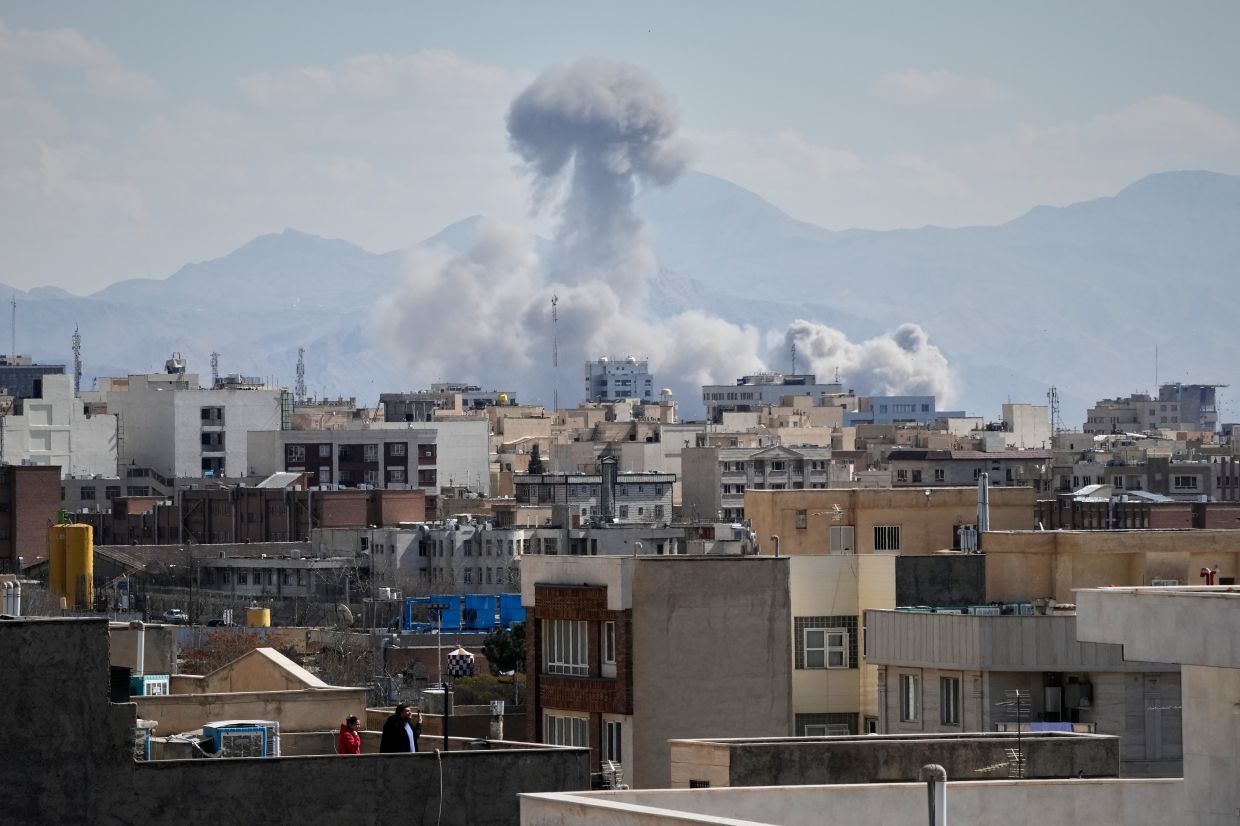 People watch from a rooftop as a plume of smoke rises after a strike by US and Israel forces in Tehran, Iran, on Sunday, March 1, 2026. -- AP Photo/Vahid Salemi