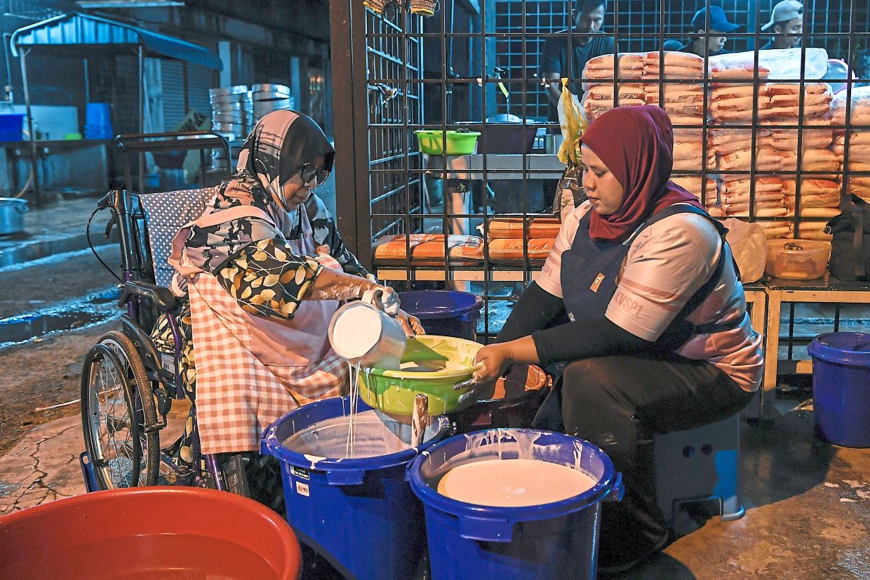 The 77-year-old, seated in a wheelchair, measuring coconut milk in preparation to make ‘kuih’ at her shop in Jitra.