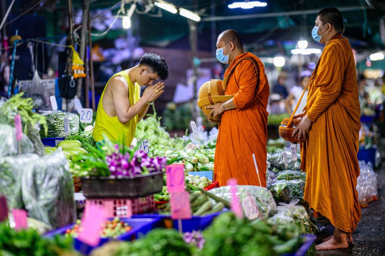 A fresh vegetable vendor gestures to monks as they collect alms at Khlong Toei Market in Bangkok early on Monday, March 2, 2026. -- Photo by ANTHONY WALLACE / AFP