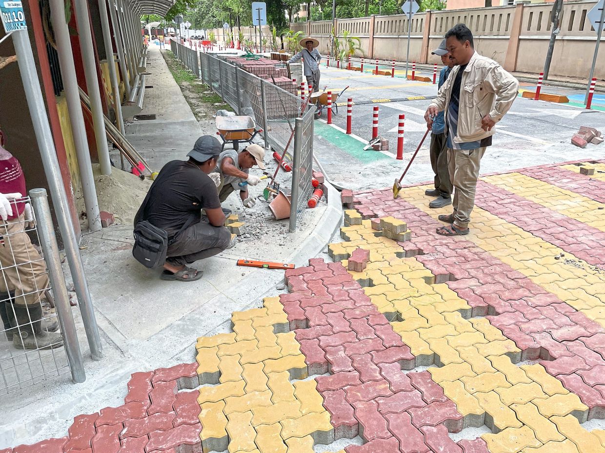 Workers reinstalling interlocking pavers along a pedestrian walkway during reinstatement works, highlighting the proper process required to restore surfaces after utility or infrastructure work. — Filepic