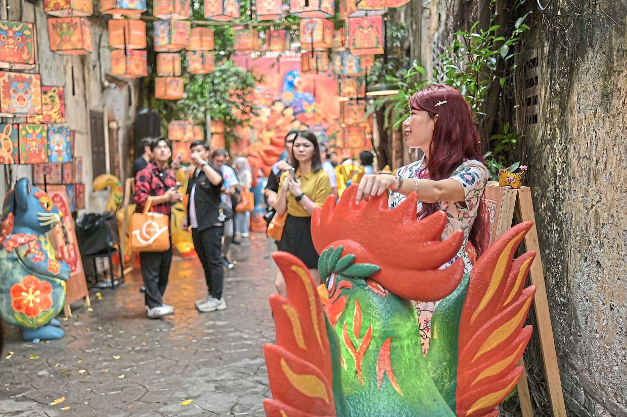 As visitors walk under the lanterns, one poses with a rooster sculpture.