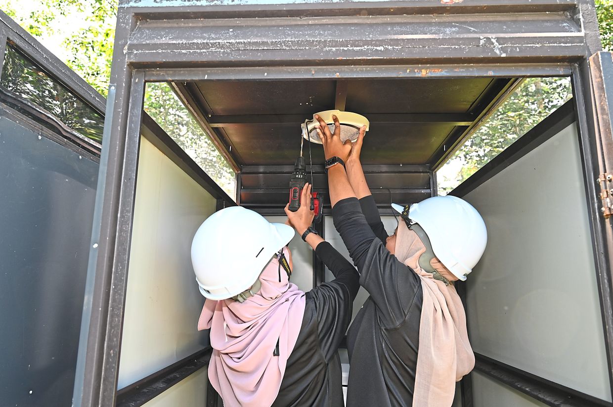 Two women volunteers installing a solar-powered light, bringing rays of hope and clean energy to Orang Asli communities.