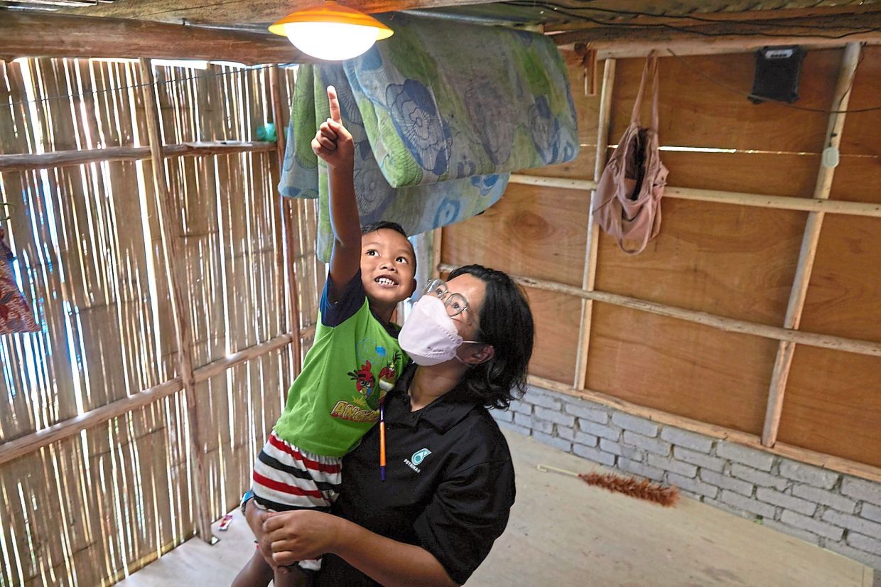 A PETRONAS volunteer shares a joyful moment as a young boy experiences the light from a newly installed solar power system.
