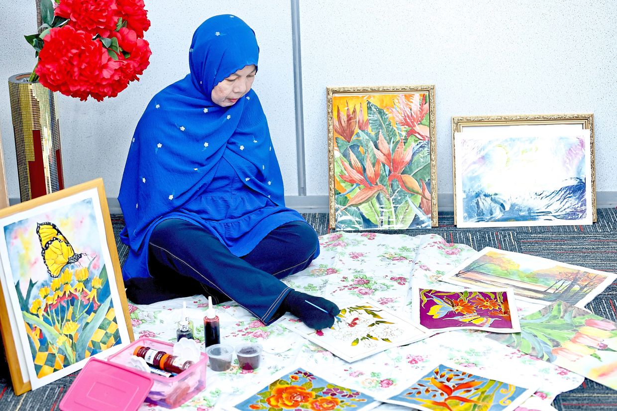 Siti Aishah painting batik pieces with her feet. Above are some of her works.