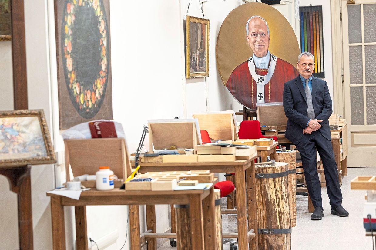 Di Buono posing for a photograph in front of a painting of Leo inside the Mosaic Studio. One of the studio’s most recent productions was a portrait of the pope, installed at Rome’s Basilica of St Paul Outside the Walls. — Reuters 
