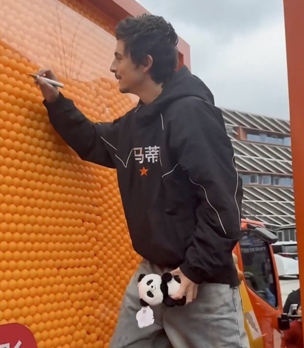 Chalamet signs a board at a public event while holding a panda toy in his left hand. -- Photo: thepaper.cn