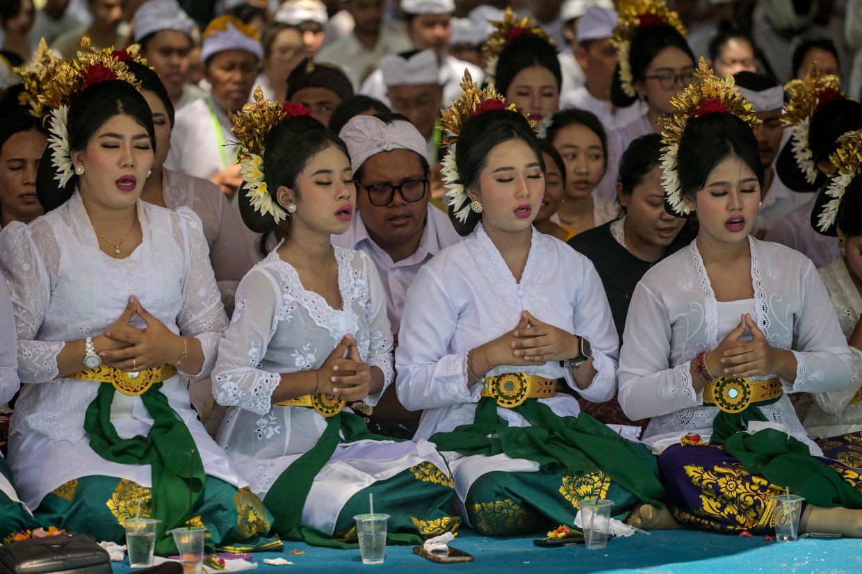 Hindu devotees pray during the Melasti ceremony prayer at Kenjeran beach in Surabaya on Saturday, March 14, 2026. Melasti is a purification festival which is held several days before Nyepi, the day of silence, when Hindu devotees are not allowed to work, travel or take part in any indulgence -- Photo by JUNI KRISWANTO / AFP