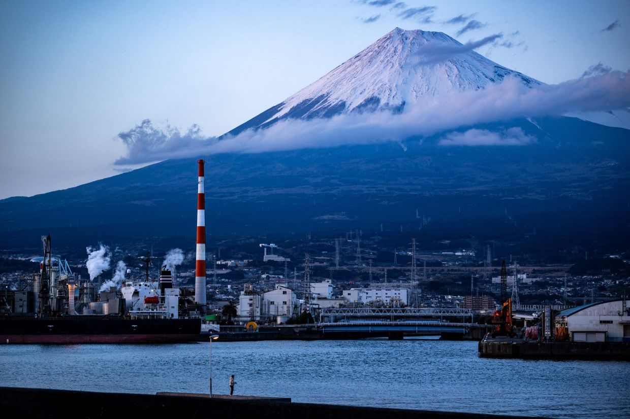 An angler fishes at Tagonoura port near industrial facilities as Mount Fuji is seen in the background from Fuji city, Shizuoka Prefecture. -- Photo by Philip FONG / AFP