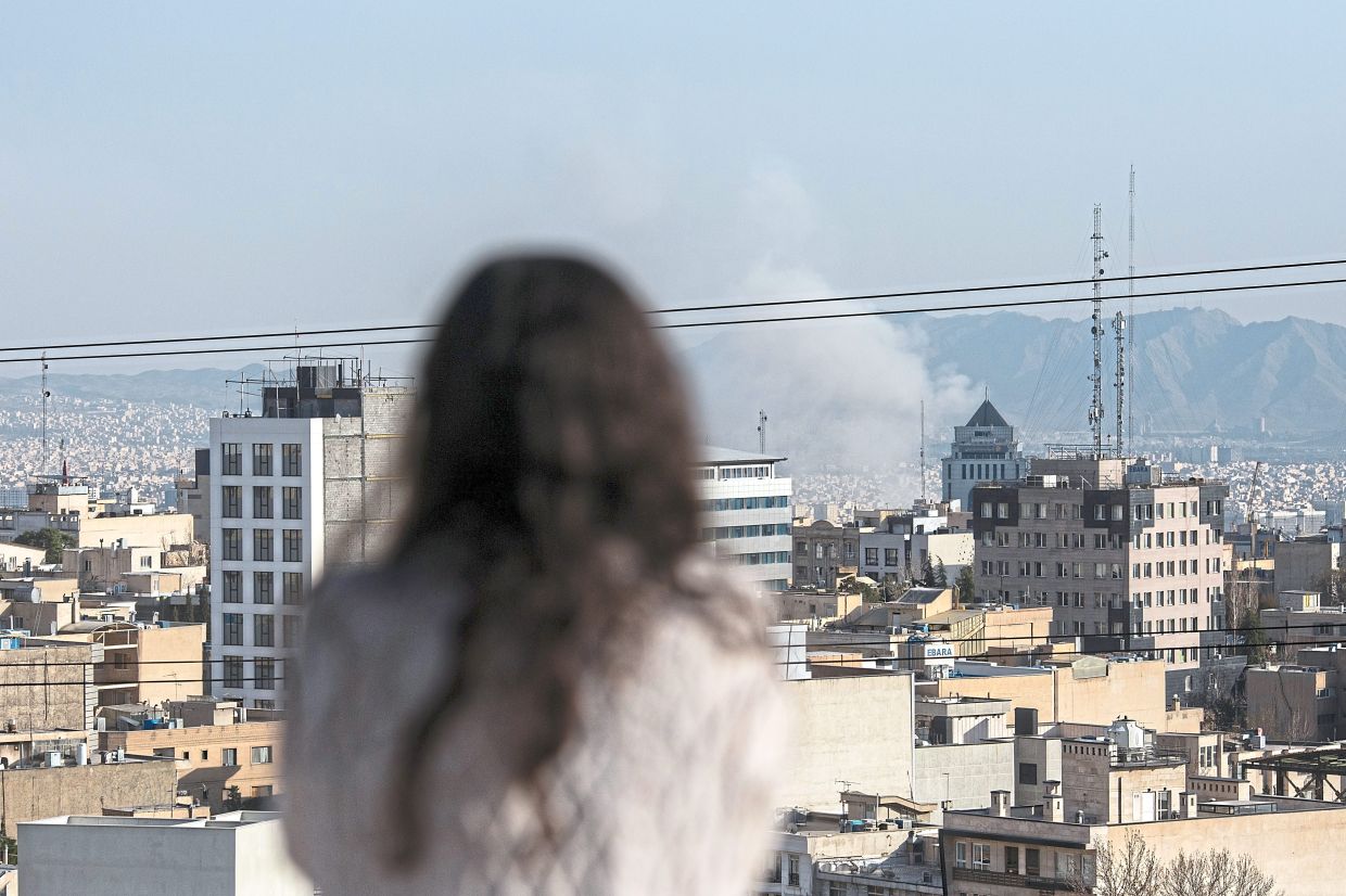A woman watches smoke rise following a missile strike in Tehran. Many Cubans are wondering if they are next. — Arash Khamooshi/The New York Times