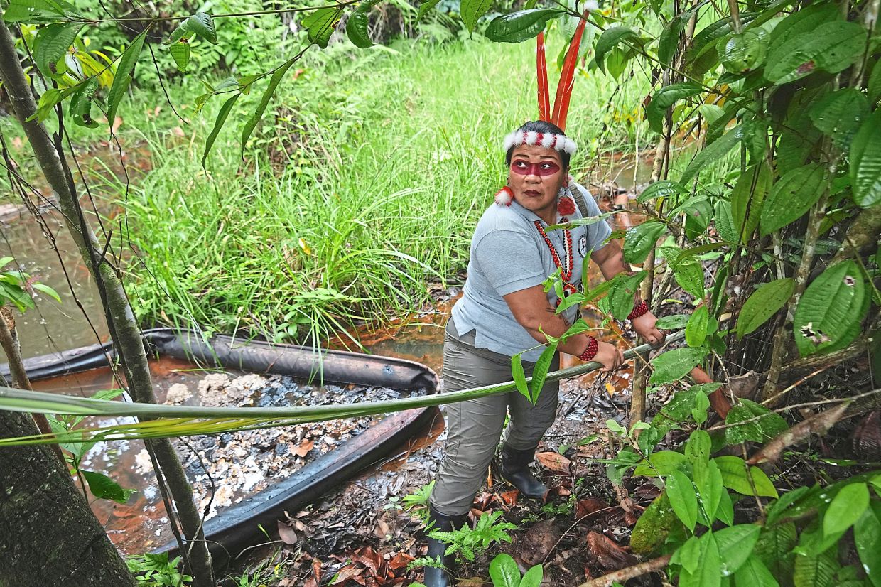Nango picking up a palm frond after wading into a darkened stream tainted by oil waste during the toxitour. 