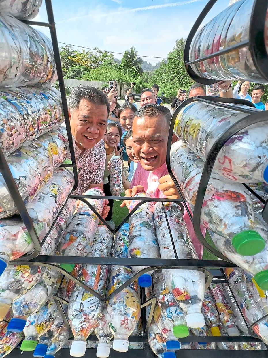 Mohd Sany (right) and Johan having a closer look at ecobricks within the metal frame of the village landmark.