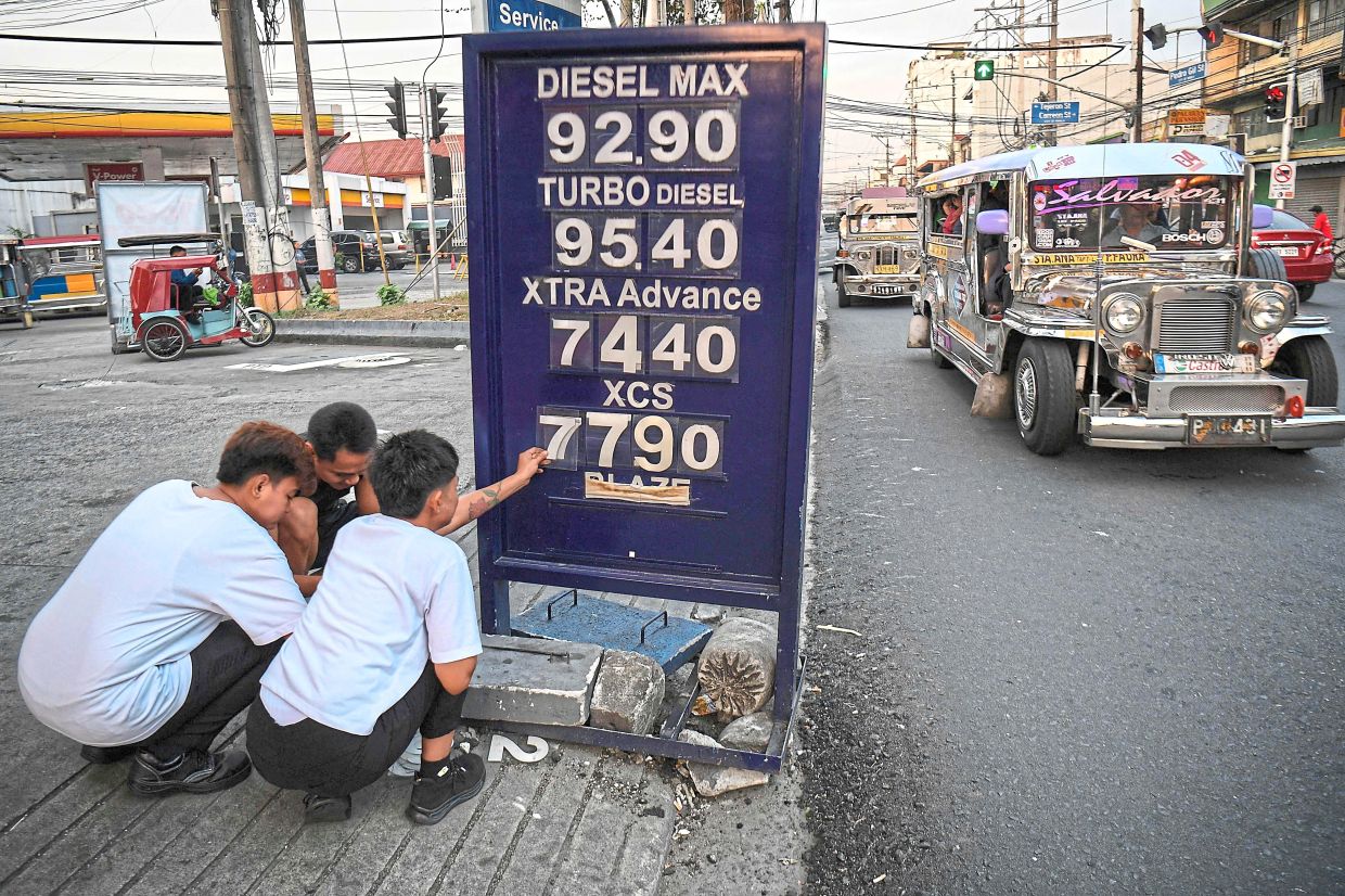 Getting higher: Workers changing the price label of fuel at a petrol station in Manila. — AFP 