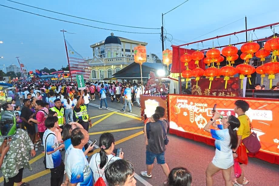 A police officer raising a “quiet” sign as the Chingay floats pass by Masjid Kampung Mahmoodiah (in the background) in Johor Baru. 