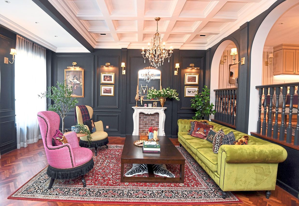 The living room with its bold black walls and strong, vibrant colours, faux fireplace and ornate decor is reminiscent of an Old Money English style.