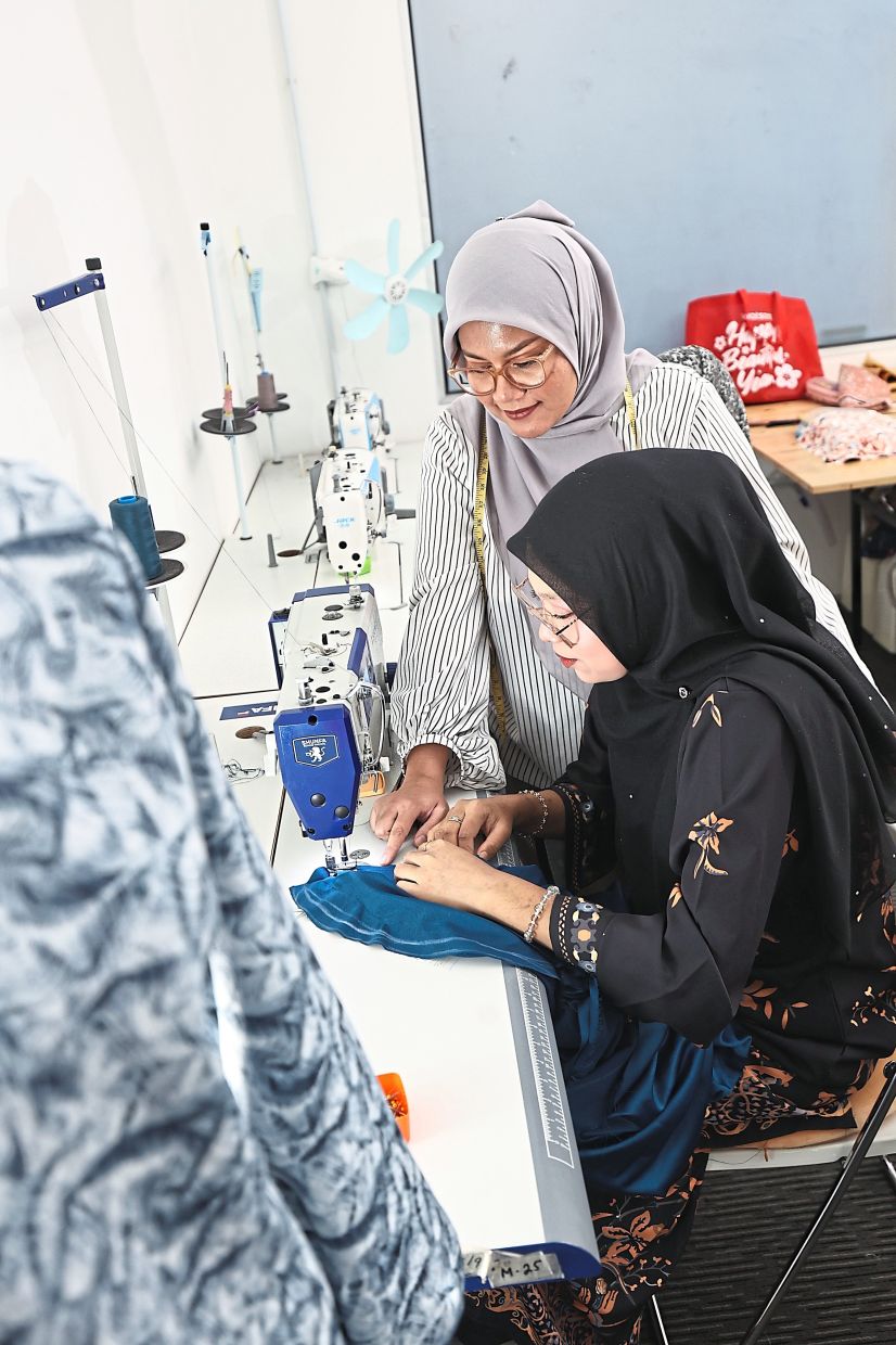 NurFatin (standing) guides one of her students on the sewing machine. Photo: The Star/Azman Ghani
