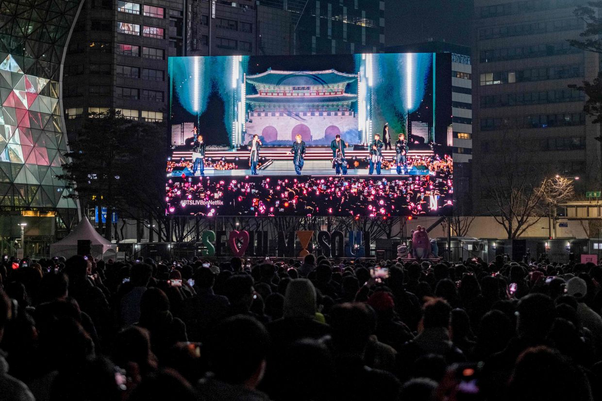 Fans watch the comeback concert of K-pop boy group BTS on a screen at the venue in Seoul on March 21, 2026. South Korean megastars BTS reunited on Saturday, March 21, for their first show in nearly four years, blowing away enormous crowds in Seoul for a K-pop extravaganza livestreamed to millions more worldwide. -- Photo by Roland DE COURSON / AFP