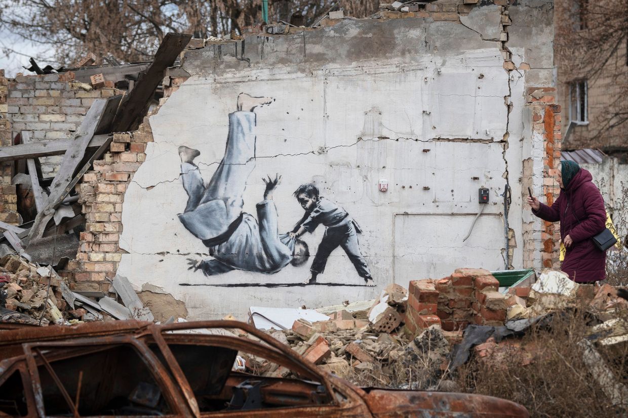 A woman takes a picture of artwork that might have been made by British street artist Banksy on a building destroyed by fighting in Borodyanka, Kyiv region, Ukraine in November 2022. Photo: AP