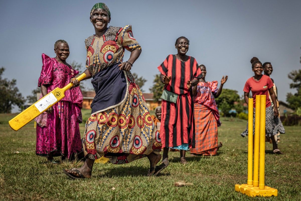 An elderly woman run between the wickets as others react during a cricket and physical training session in Jinja, on January 10, 2026.