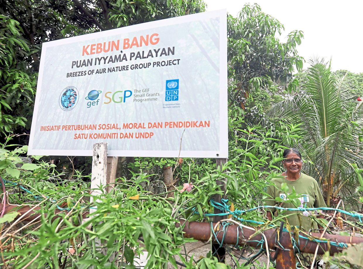 Iyyama at her garden plot with a sign bearing the BANG project in Klang.