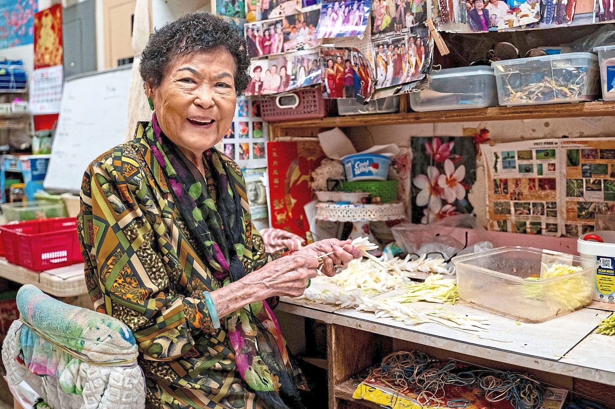 Cindy Lau, owner of Cindy’s Lei Shoppe, threading flowers onto string to make lei in Honolulu’s Chinatown.