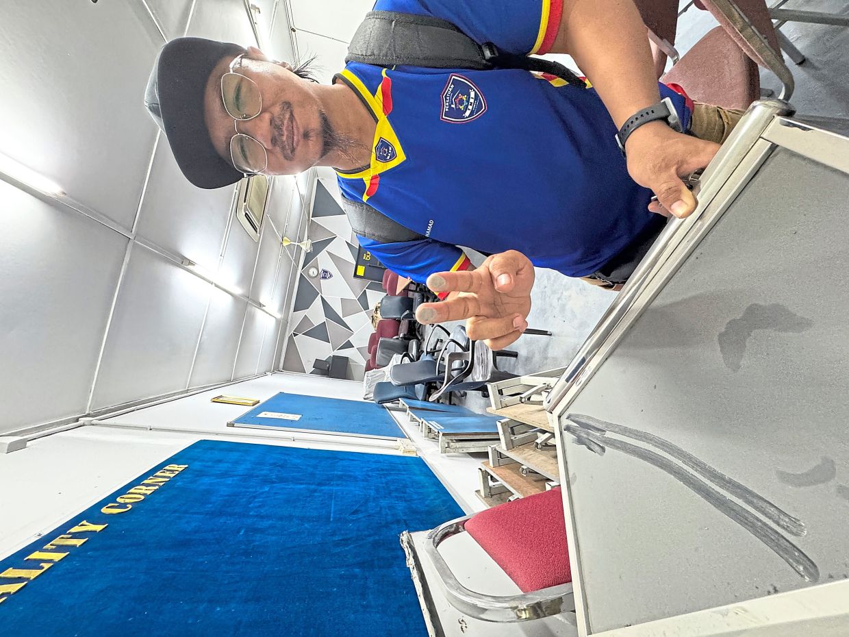 Muhamad showing dust on furniture in the Taman Matang Jaya community hall.
