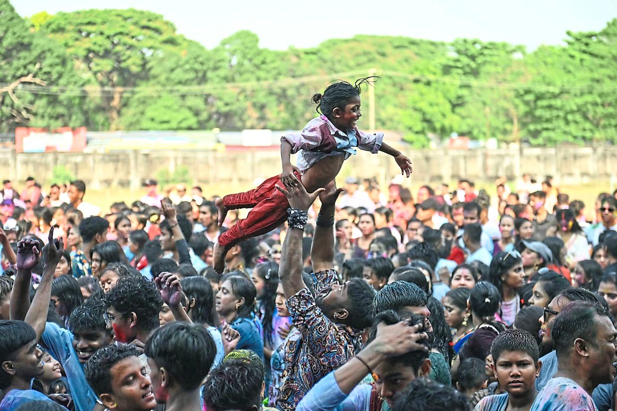 3. A man lifting a child into the air as Hindu devotees covered in coloured powder celebrate Holi in Yangon, Myanmar. — AFP