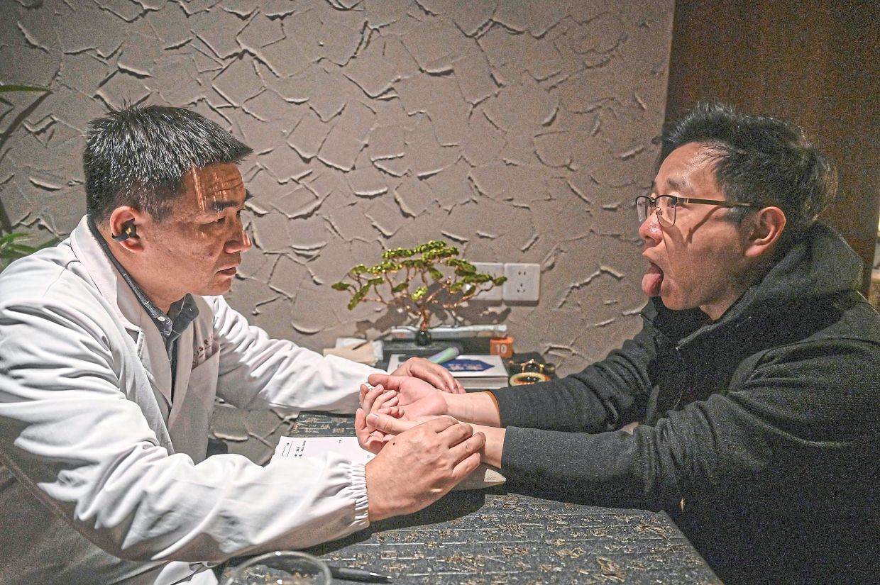 Chinese medicine practitioner Ding (left) performing a pulse diagnosis on a customer at Niang Qing. — AFP