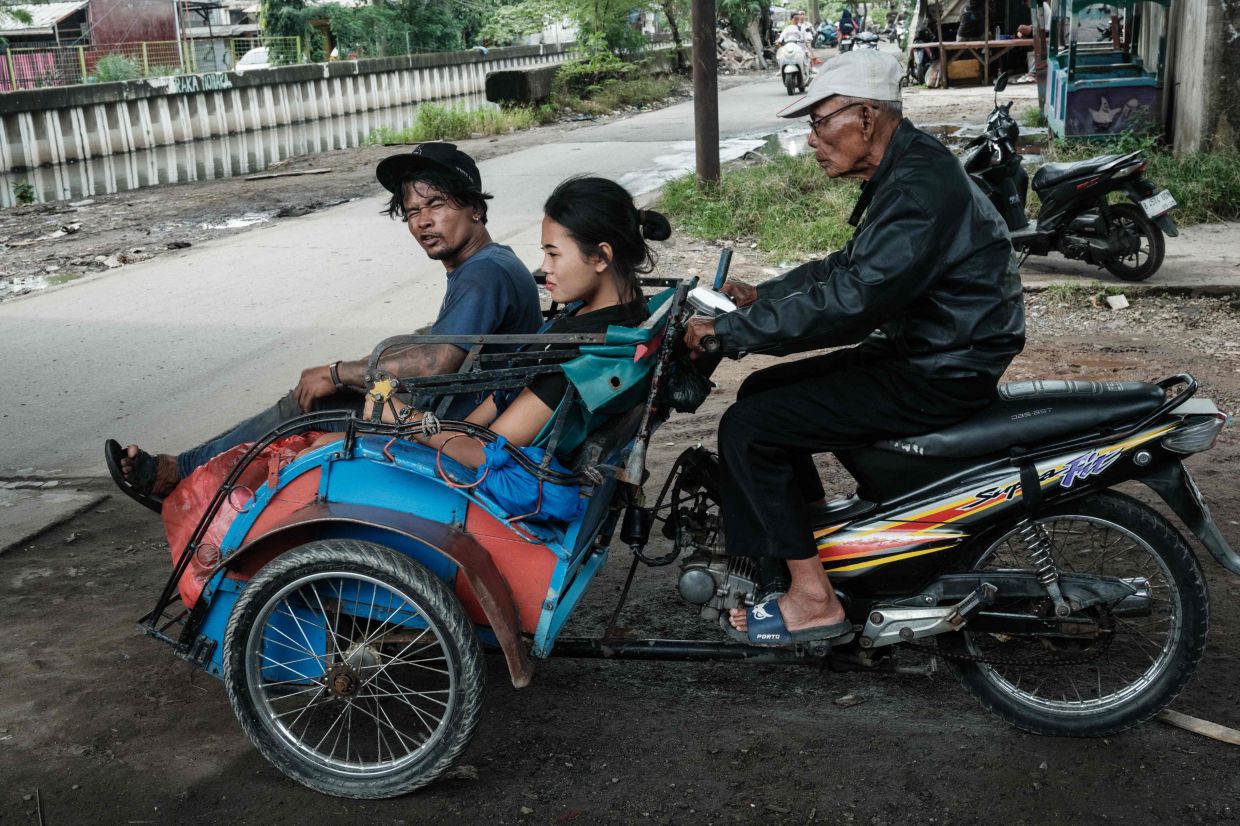 A motorcycle converted into a tricycle carries passengers in Jakarta. -- Photo by YASUYOSHI CHIBA / AFP)