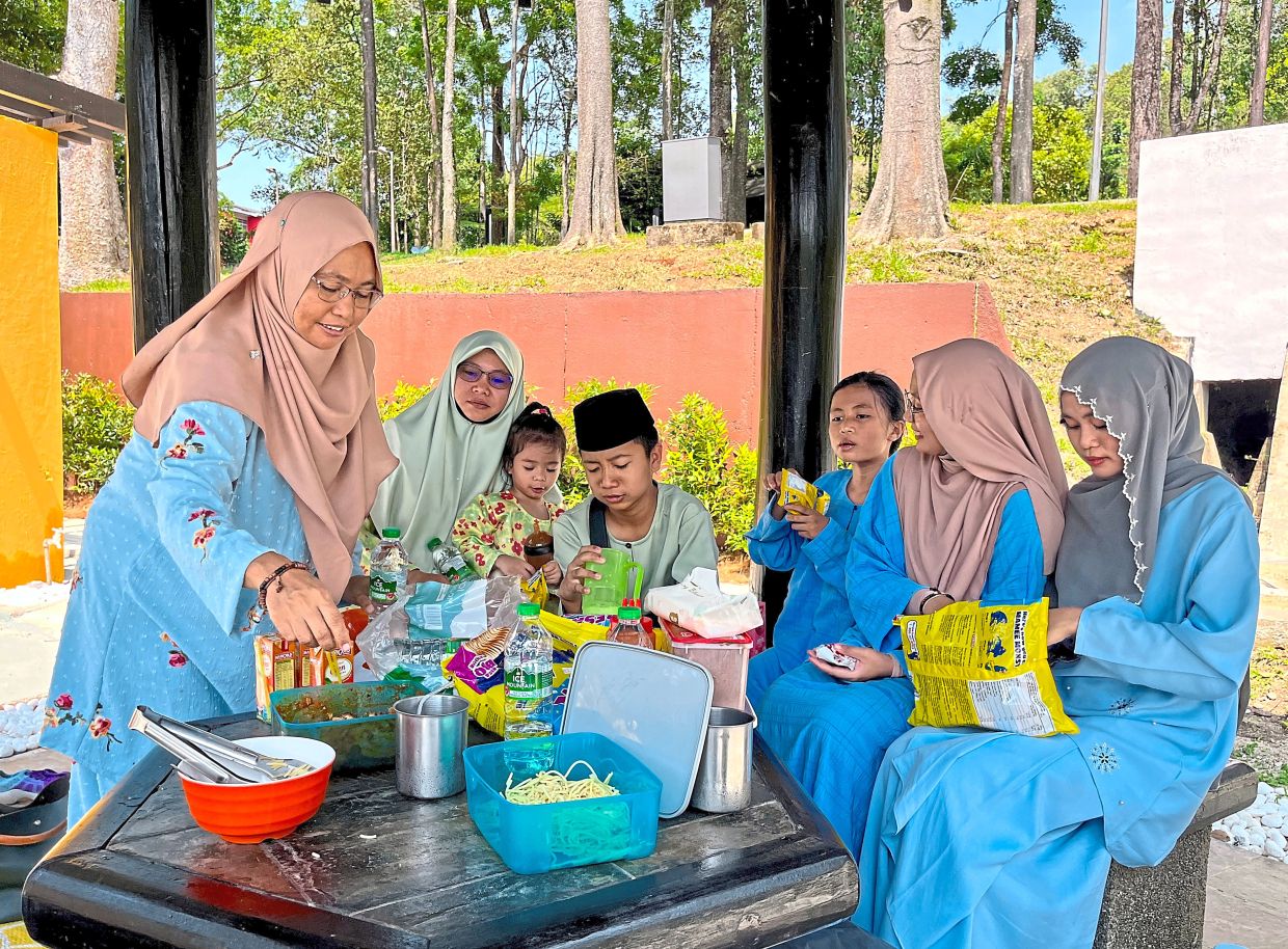 Siti Arvina (left) and her family, all dressed in their Raya outfit, enjoying a picnic at the park. — Yee Xiang Yun/The Star