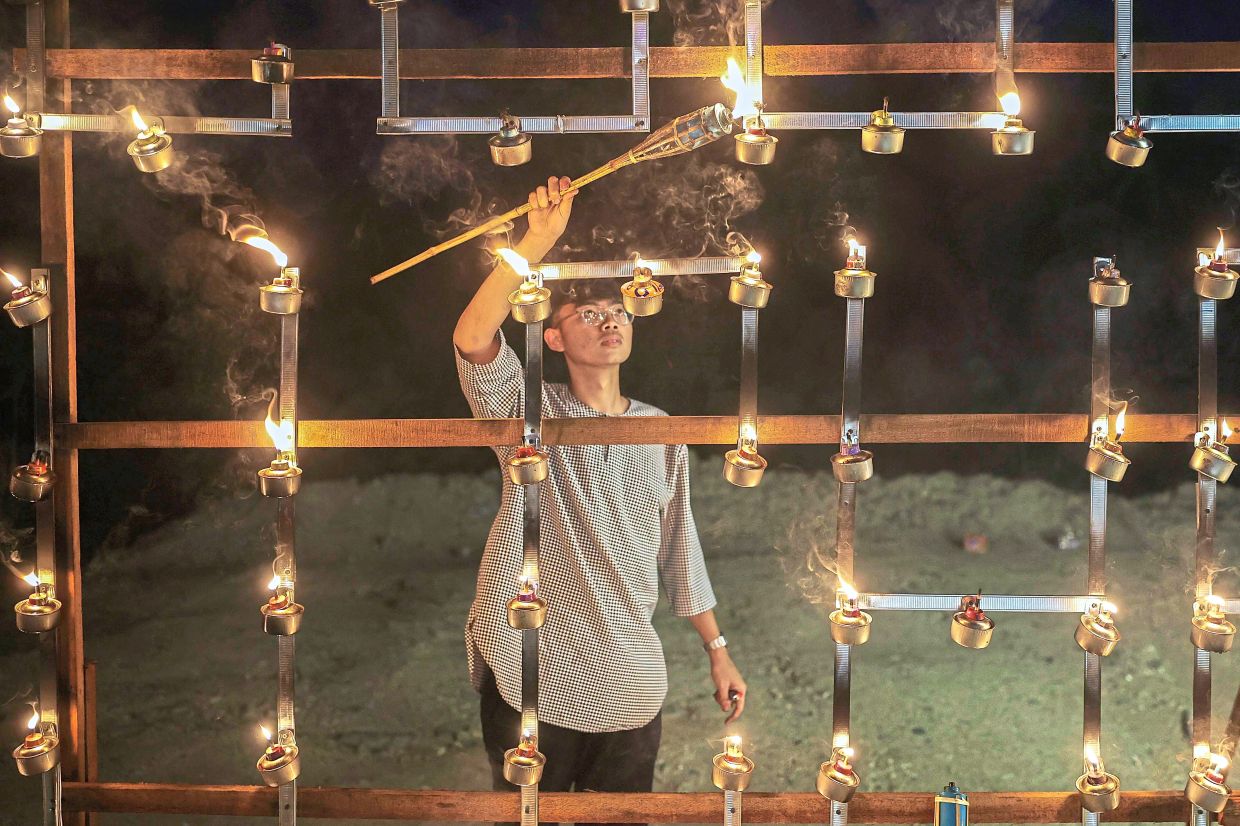 A participant carefully lighting a row of pelita, bringing the festive display in his village to life.