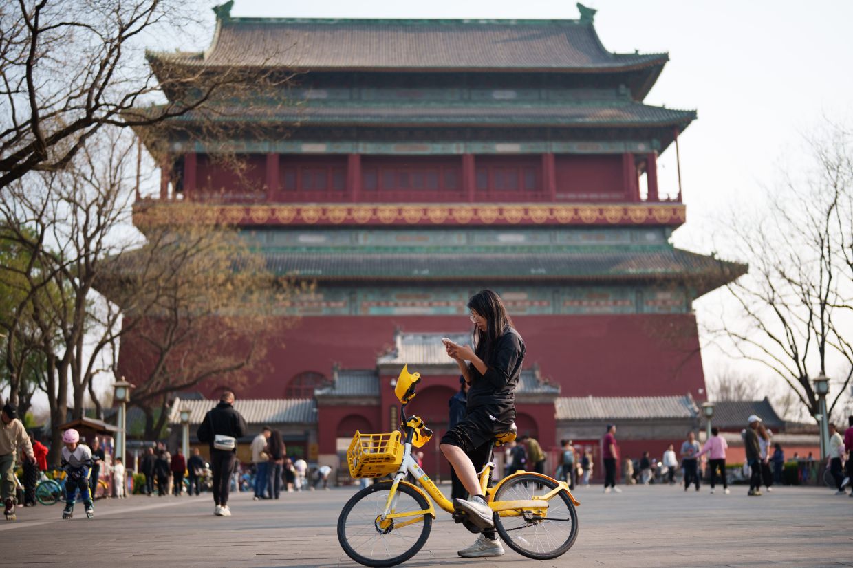 A teenager looks at her phone during a riding outing at the Drum Tower in Beijing, China, on Tuesday, March 31, 2026. -- AP Photo/Vincent Thian