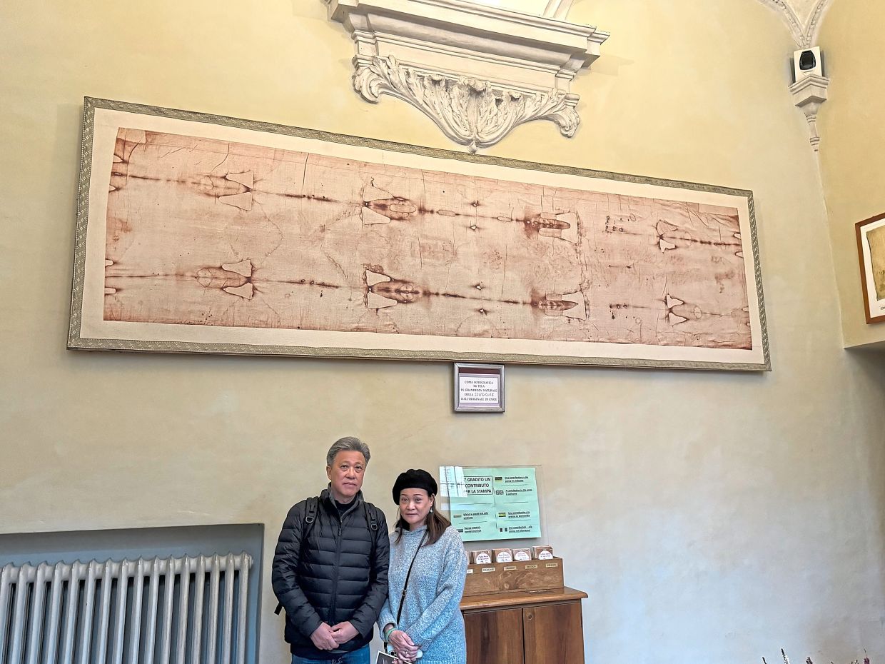 The writer and his wife inside the church office, with a replica of the Shroud of Turin hanging on the wall. — FLORENCE TEH