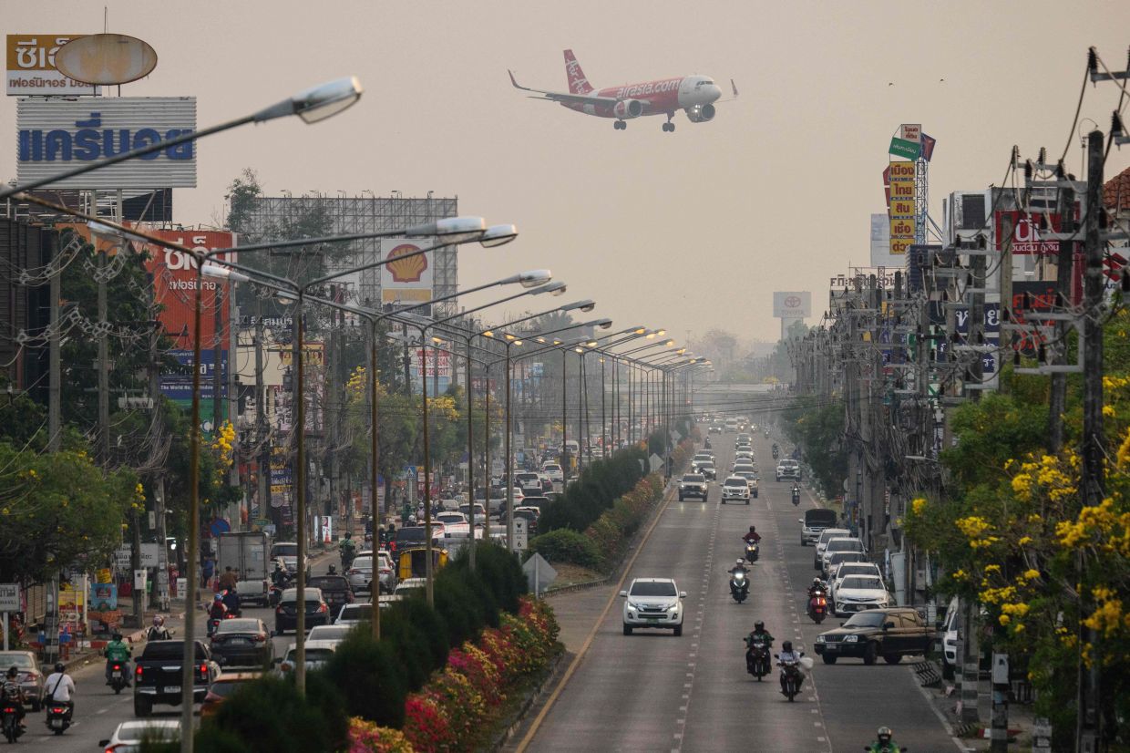 A passenger plane preparings to land at the airport as commuters drive on the road below on a heavily polluted day in Chiang Mai on April 2, 2026. Seasonal agricultural burning, forest fires and weather patterns produce an annual pollution season across much of South-East Asia. But parts of northern Thailand are seeing haze that even hardened locals say is exceptional. - AFP