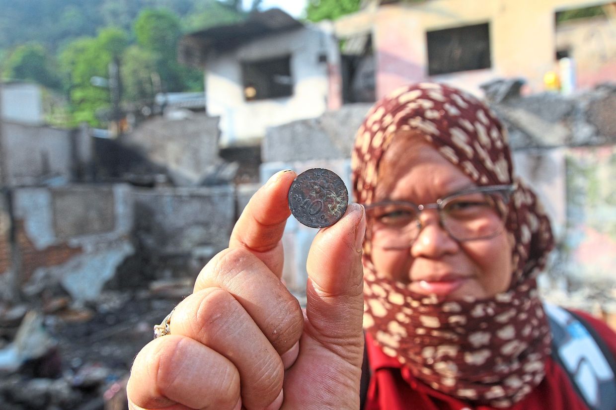 Rosmawati holding up a 10sen coin recovered from the debris. The family lost RM20,000 kept at home for a family ‘kenduri’.