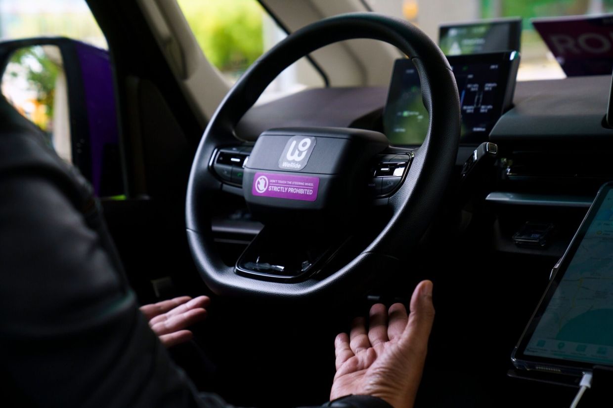A safety officer in the driver's seat on board a GRX robotaxi, operated by Grab Holdings Ltd. and WeRide Inc, in Singapore. Singapore's Grab became Southeast Asia's first ride provider to start a driverless service, betting the technology can help cut costs and prove out robotaxis in dense urban traffic. -- Photographer: Ore Huiying/Bloomberg