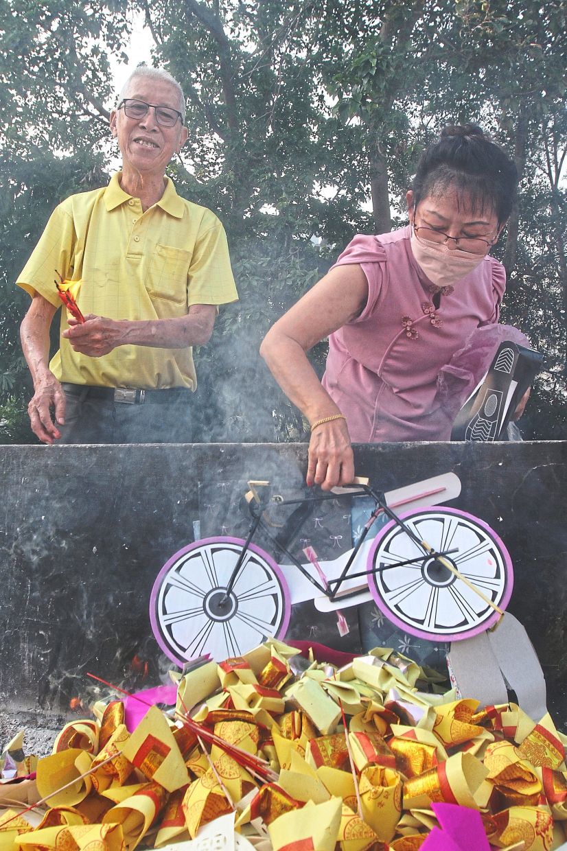 Devoted: Hee looking on as his wife Khoo Poh Lai places the joss paper bicycle he bought to burn for his father at the cemetery and columbarium in Tanjung Tokong, Penang. — LIM BENG TATT/The Star