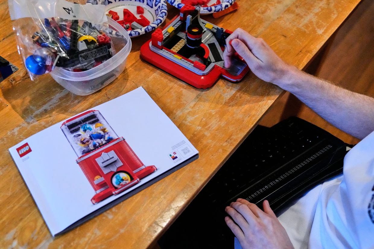 Matthew Shifrin reads from a braille terminal while building the Lego Mini-Figure Vending Machine set.