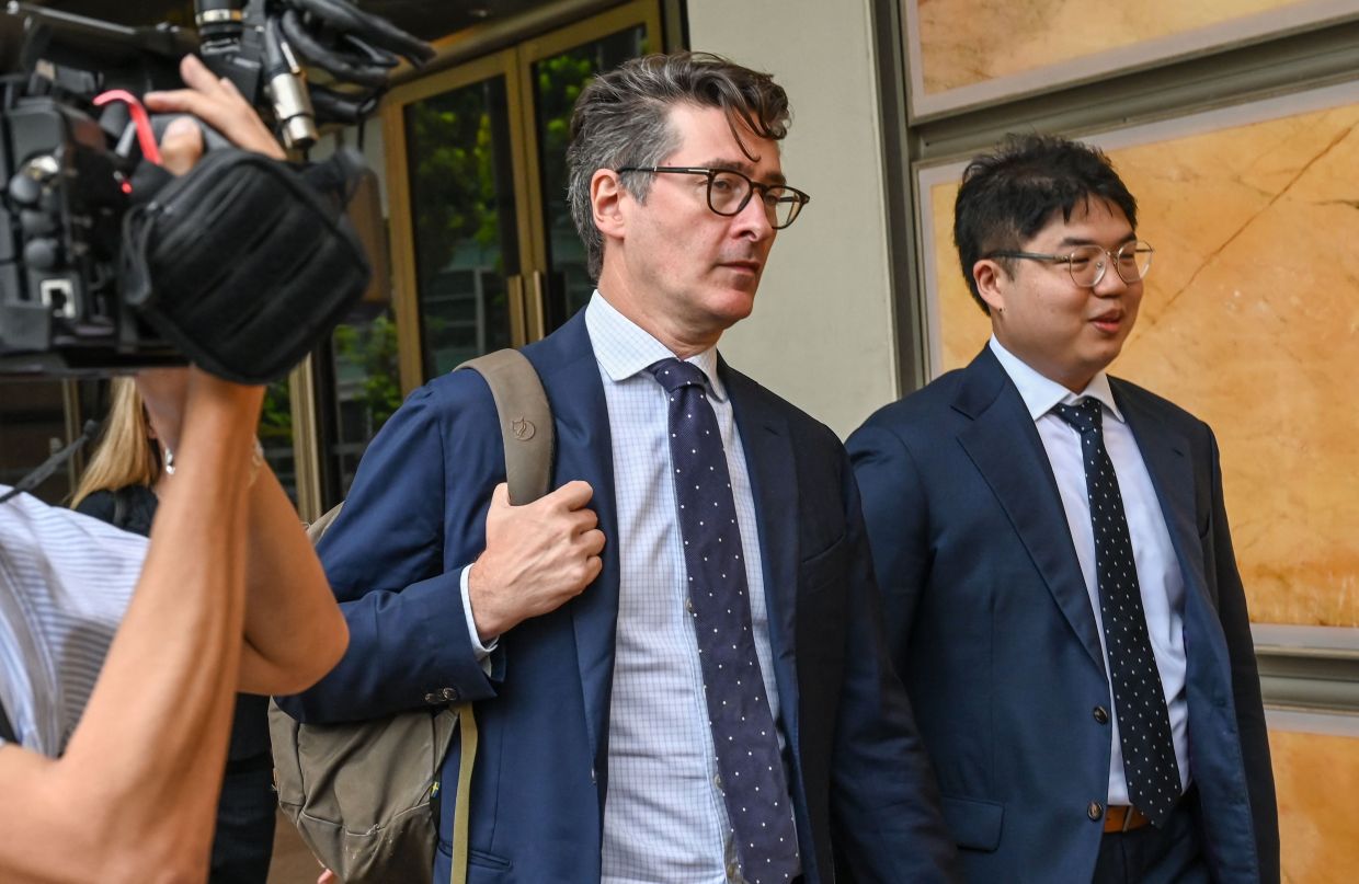 Singapore-based Bloomberg News senior executive editor John Fraher (centre) and reporter Low De Wei (R) leave the Supreme Court in Singapore on Tuesday, April 7, 2026. -- Photo by Roslan RAHMAN / AFP