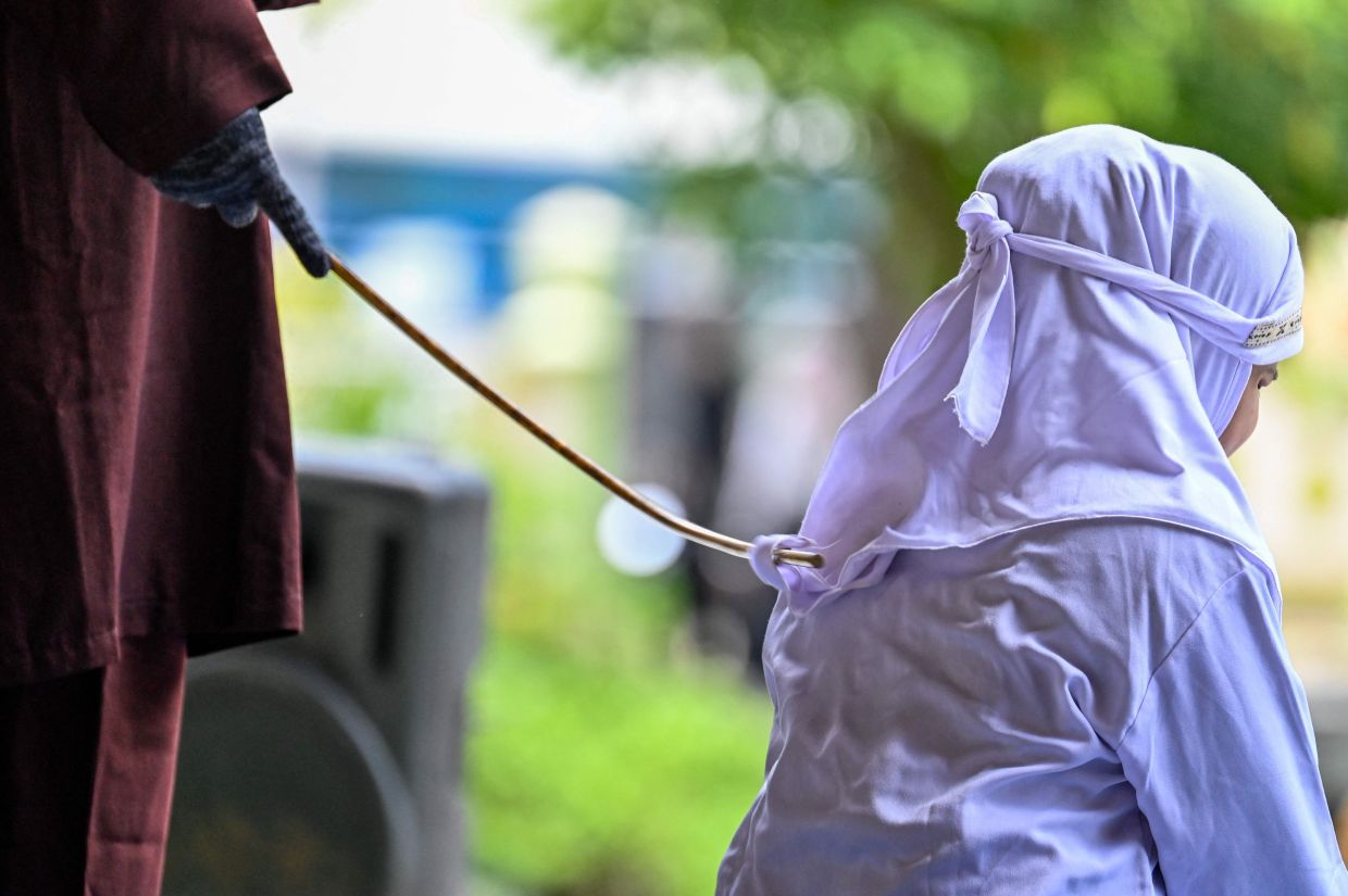 A woman (right) reacts during a public flogging held by Aceh's Sharia police in Banda Aceh on Tuesday, April 7, 2026. A couple was publicly flogged in Indonesia's staunchly Islamic Aceh province on April 7 for having sex outside of marriage, an AFP reporter witnessed, in the country's only region to apply a version of Sharia law. Sexual relations between unmarried people are outlawed in Aceh. -- Photo by CHAIDEER MAHYUDDIN / AFP