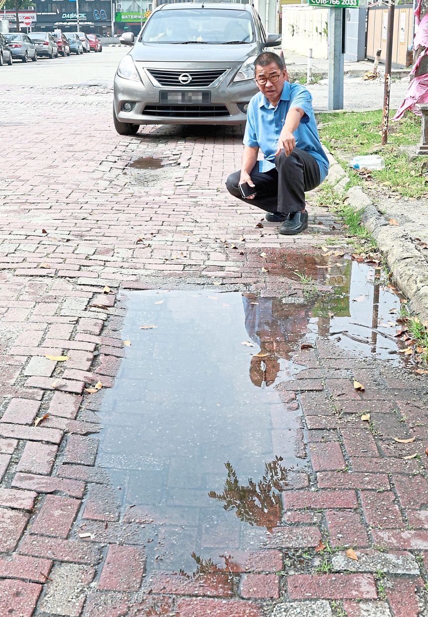 Yee pointing out a water-filled sunken patch on an interlocking brick road at Fortune Square in Kepong.