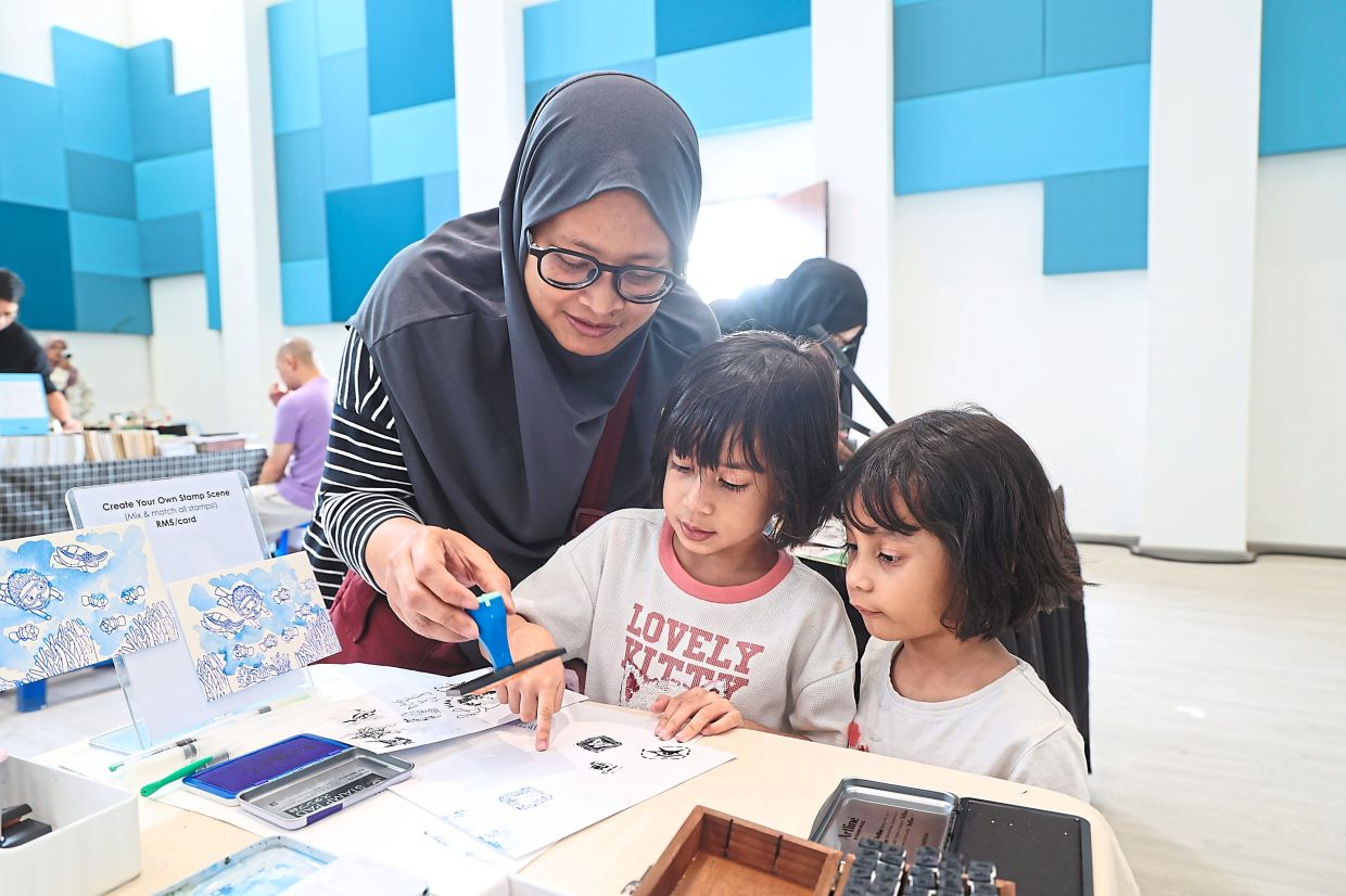 Nor Diyana showing her daughters how to use rubber stamps at the secondhand book market.