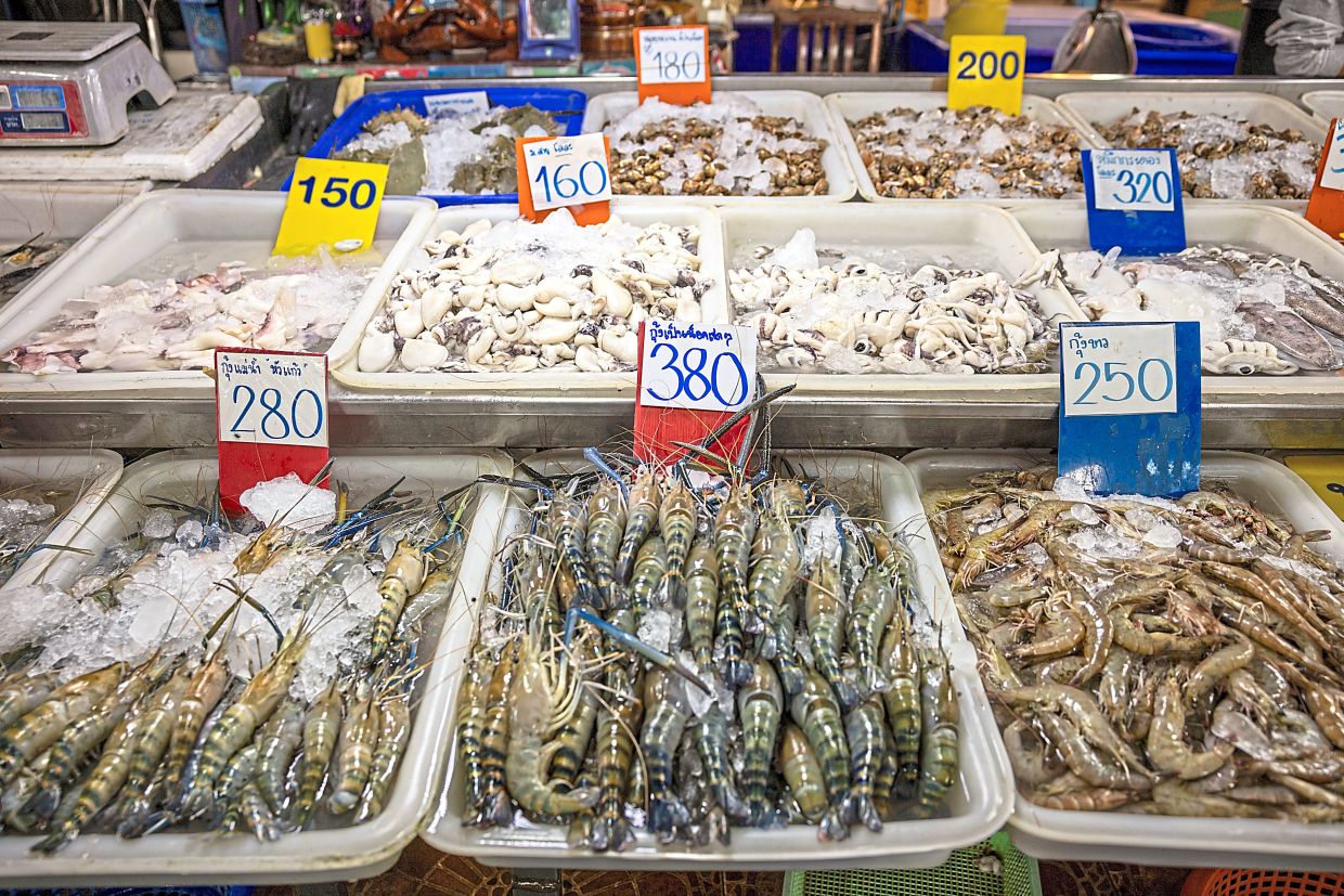 (From left) A seafood market in Samut Sakhon, and fishermen performing maintenance on the shrimp boat ‘Lucky Blessing’ while docked where supplies are threatened by the effect of rising diesel prices on fishing. — Lauren DeCicca/The New York Times