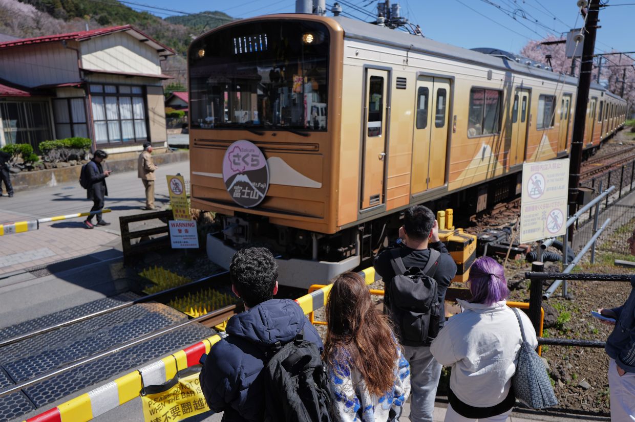 Foreign visitors looking at a train passing through a railroad crossing near Shimoyoshida Station. 