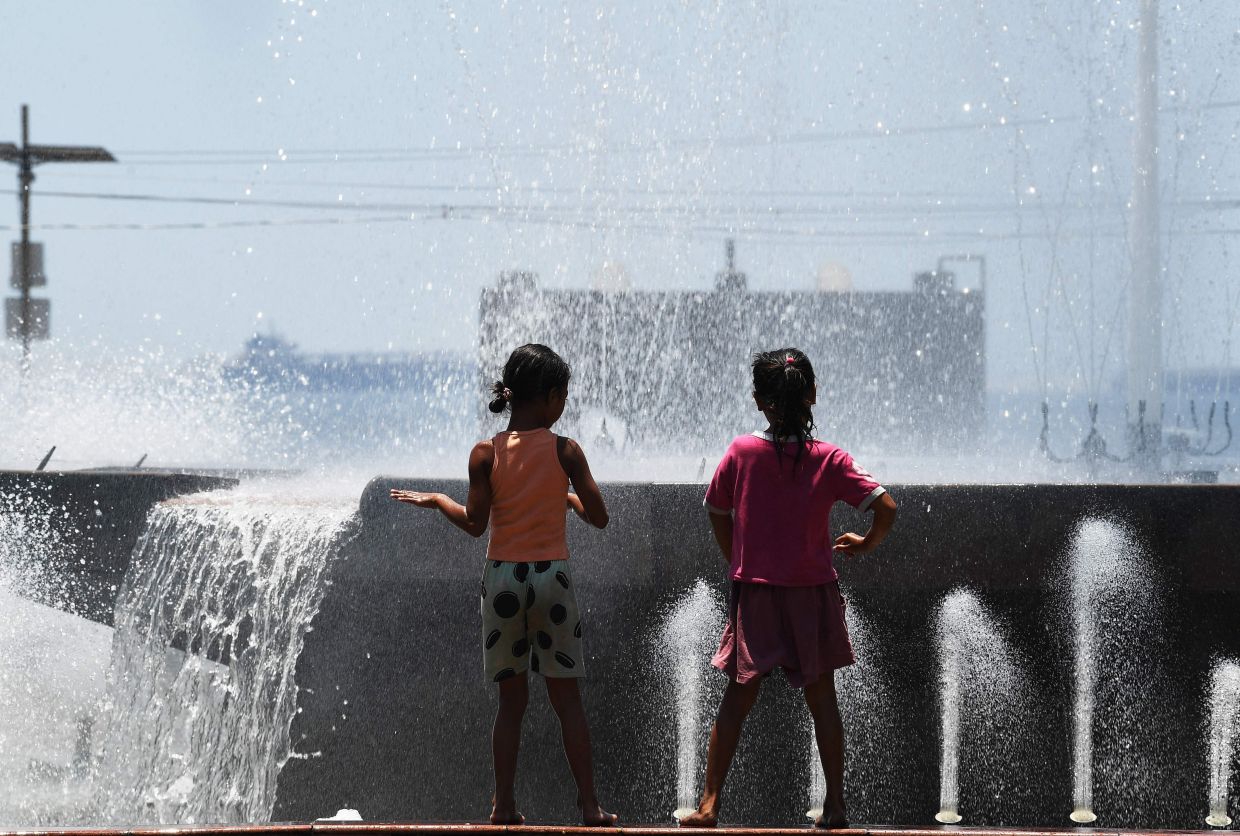 Young girls cool off on a fountain next to a park in Manila as temperatures rose in the metropolis, with the weather bureau warning residents of the dangers of heatstroke due to prolonged exposure to heat. -- Photo by Ted ALJIBE / AFP