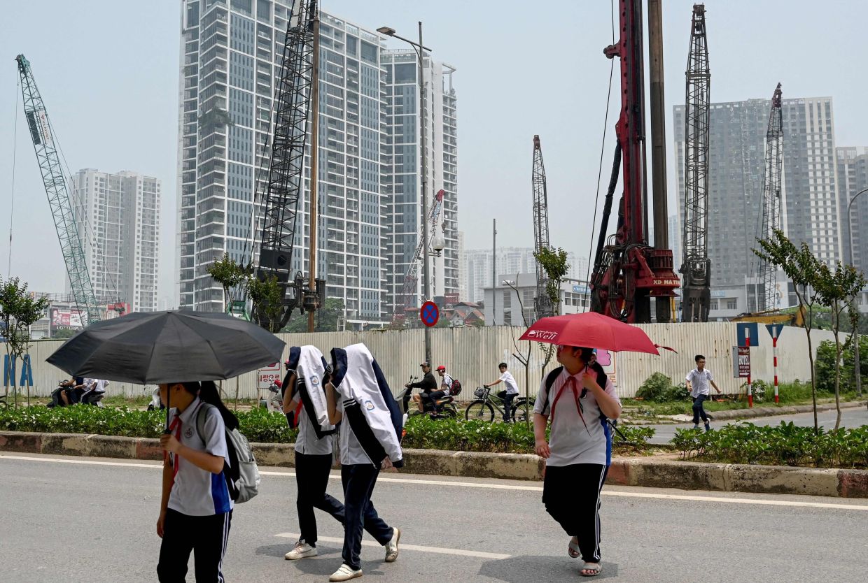 High school students use umbrellas and jackets to shield themselves from the heat while crossing a street near a construction site in Hanoi. -- Photo by Nhac NGUYEN / AFP)