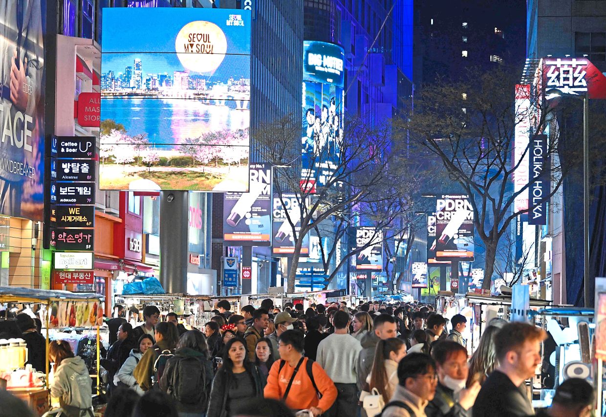 People walk beneath digital billboards at Myeongdong shopping district in Seoul on April 1, 2026. — Photo by Jung Yeon-je / AFP