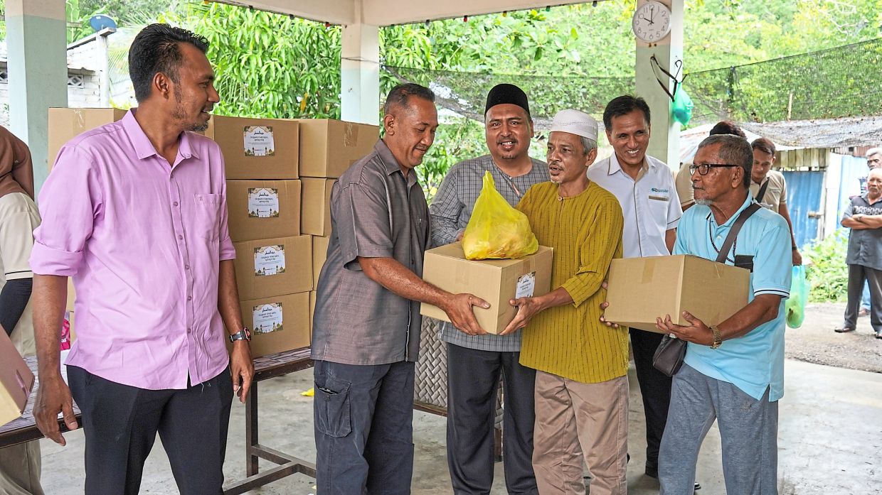 Khairi (second from left) presenting food boxes to fishermen witnessed by (from left) Mohd Aidil Fitri, Azrul Mahathir and Azmi. — Courtesy photos