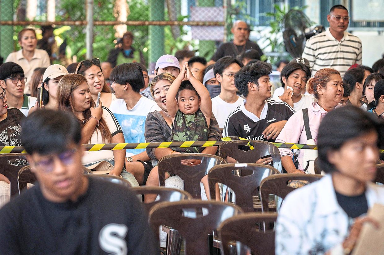 Luck of the draw: Relatives looking on as a man draws his ballot during the Thai military conscription lottery. — AFP