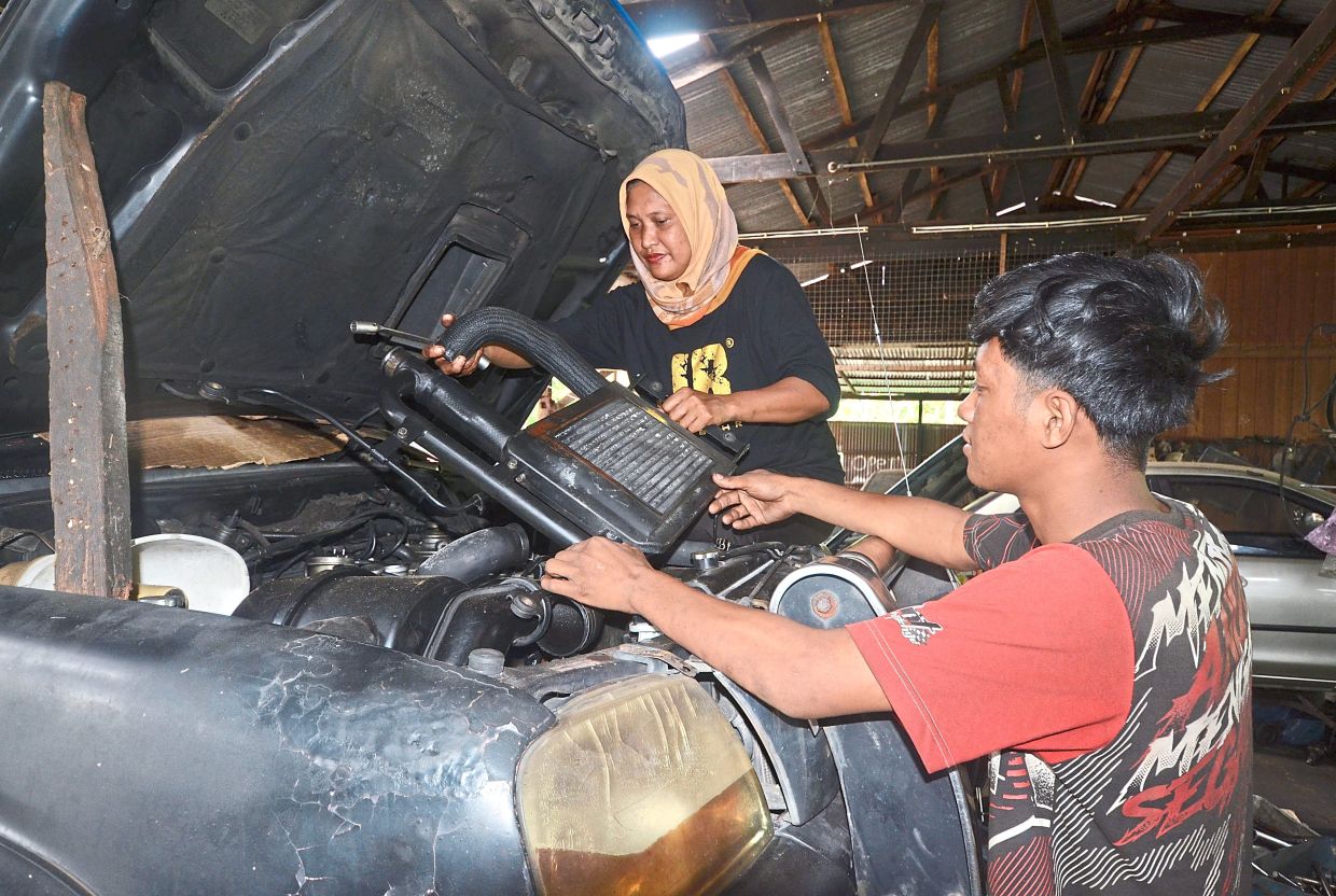 Being assisted by son Muhammad Azani while working on a four-wheel-drive vehicle. — Photos: Bernama